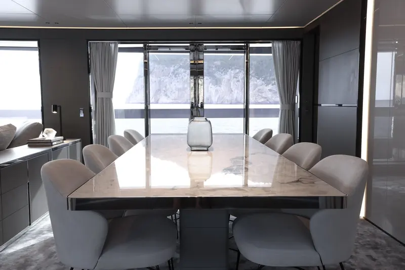 The main-deck dining table seats ten under a marble top, framed by floor-to-ceiling doors onto the aft deck.