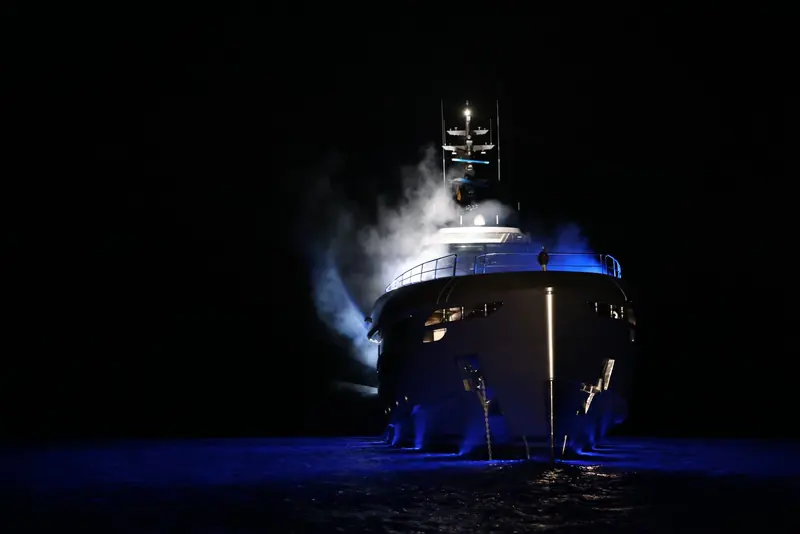 Departing at night under her underwater lighting, bow thrusters throwing spray lit blue against the dark.
