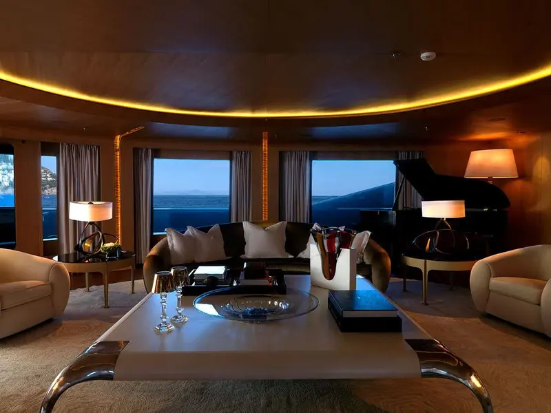The main salon runs the full beam with a baby grand piano set against the window line, upholstered in a warm, tailored palette rather than the cooler tones common on newer tonnage.
