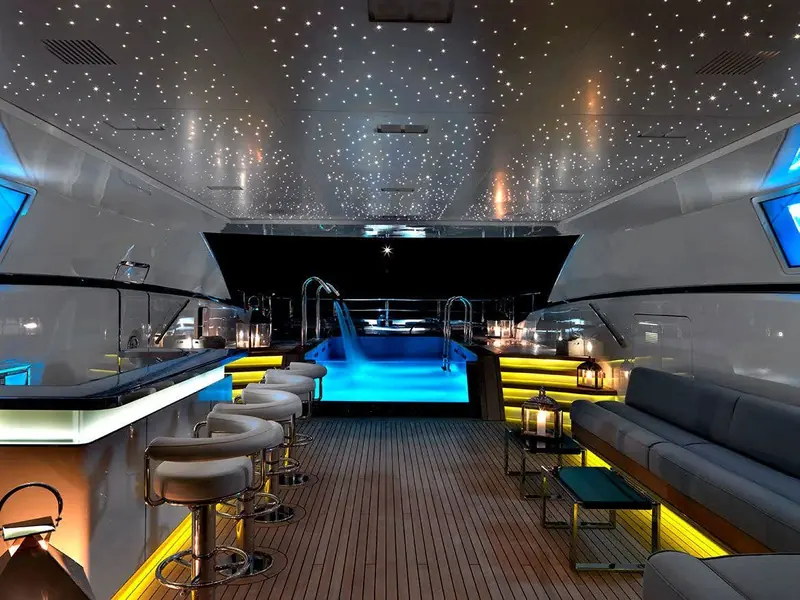 The lower pool deck lit at night, with a star-pattern fibre-optic ceiling over the plunge pool and integrated bar seating built into the hull sides.