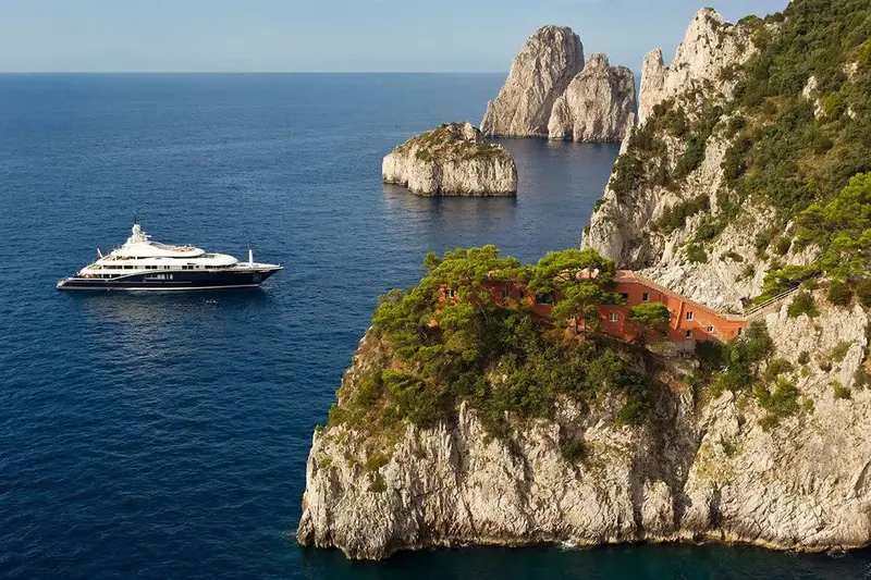 Numptia at anchor beneath Capri's cliffs near the Faraglioni, giving a sense of true scale against the island's rock face that a dockside shot cannot.