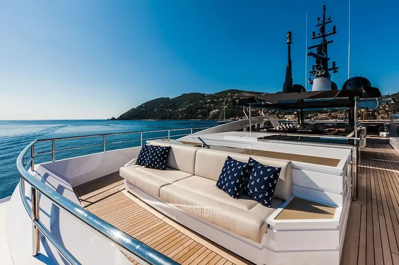 A foredeck sofa with a coastal town visible off the bow, the mast and radar arch towering behind.