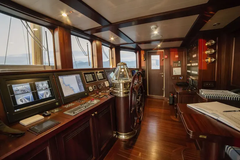 The wheelhouse pairs a traditional wood-and-brass wheel and binnacle with modern chartplotters and CCTV monitors.