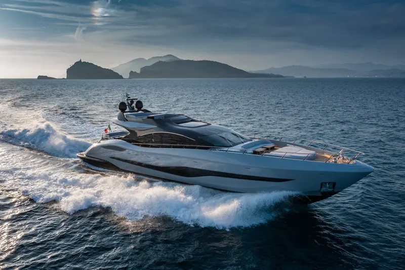 The 132E running past the Portofino headland in low evening light, her hard-chine planing hull throwing a wide, flat wake typical of Mangusta's high-speed open line.