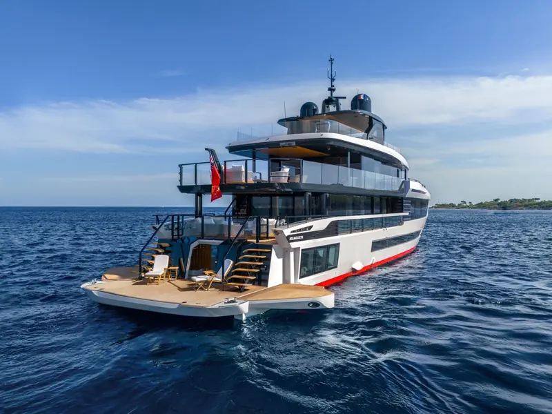 Stern view at rest with the boarding ladder down and the French ensign flying - the flybridge overhang shelters the aft cockpit seating below it.