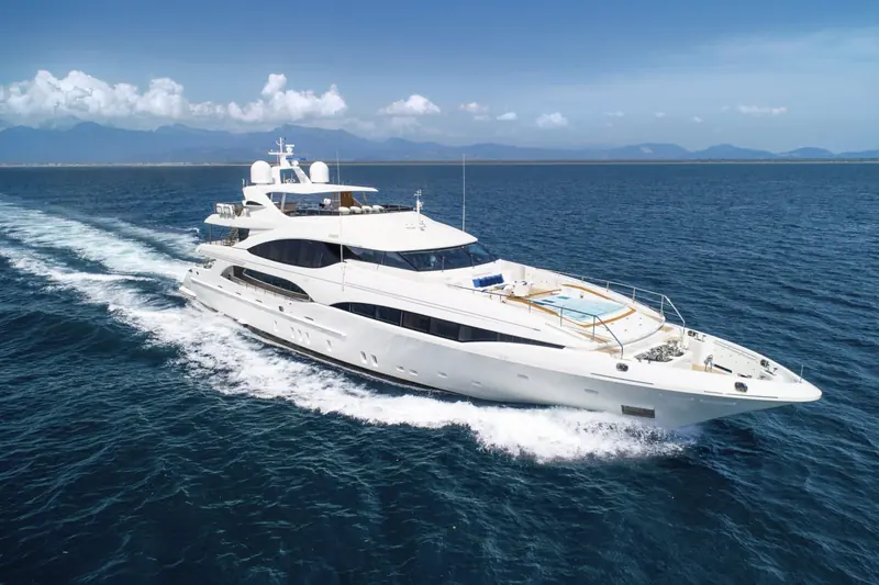 Mangusta Oceano 46 underway off a mountainous coastline, the drop-down bow terrace and foredeck sunpads visible ahead of the raised wheelhouse.
