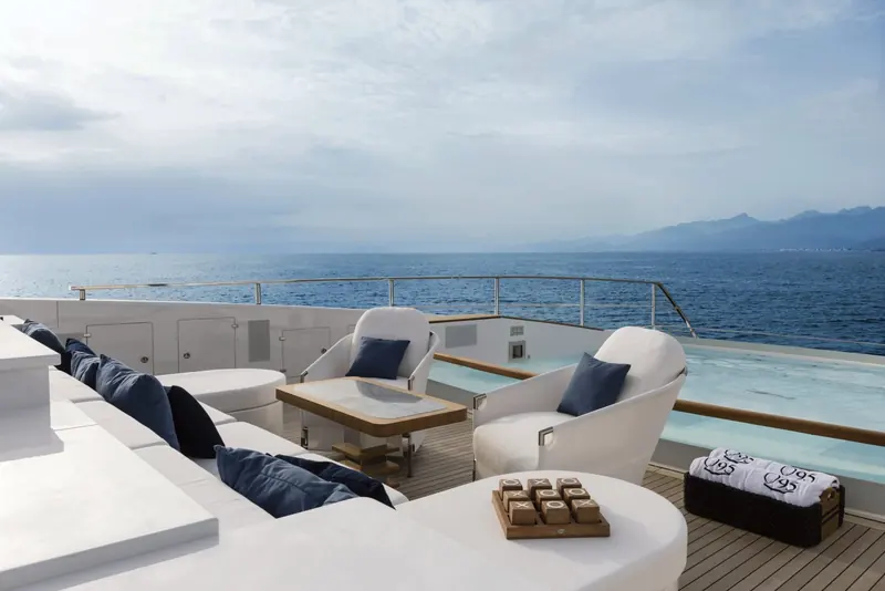 Upper-deck lounge seating open to the sea on three sides, cushioned in navy against white upholstery.