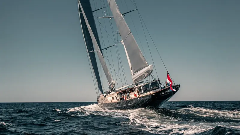 Aquarius under sail, her black hull and Bermudan ketch rig cutting a clean wake with the mizzen carrying its own genoa.