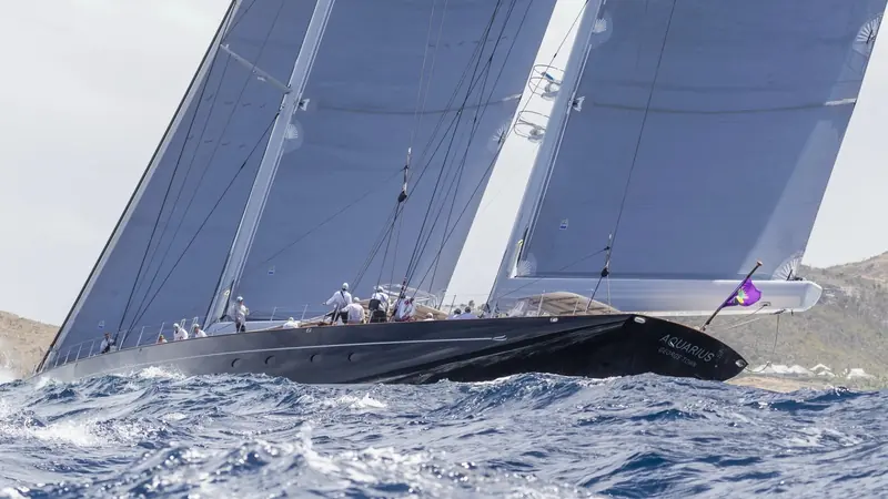 Racing another yacht upwind, crew visible on the rail, the purple burgee at the masthead identifying her among a fleet of similarly dark hulls.