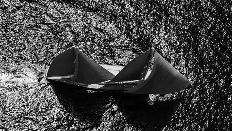 An extreme overhead close-up on the black sails alone, the weave and trim of the cloth visible against the water.