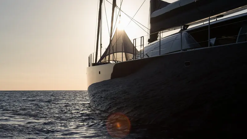 Bow-on at sunset, the low sun catching the sheer of the topsides as she comes up to a mooring.