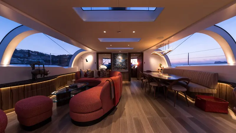The saloon at dusk, a bronze rhino sculpture and a full dining table showing an interior built for living aboard rather than a boat-show mock-up.
