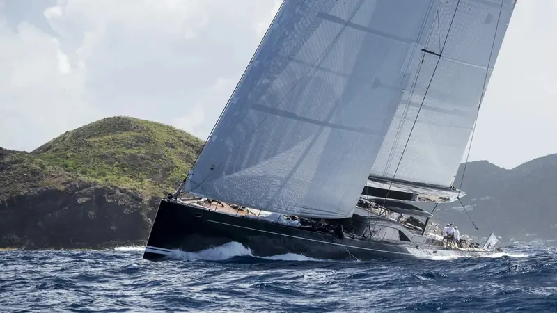Passing the cliffs of a Caribbean island, canting keel and carbon rig driving her hard on the wind.
