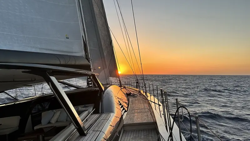On deck at sunset, the cockpit's carbon coamings and teak underfoot lit low and gold, instruments reading speed and heading to port.