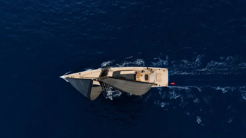 Directly overhead under sail, the red lifebuoy at the stern the only spot of colour against the black hull and the deep blue of open water.