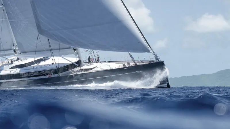 Heeled hard into a swell, spray coming green over the rail - the black hull and low freeboard were drawn for genuine sailing performance, not static anchorage looks.