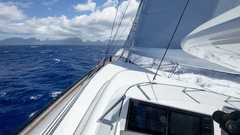 Looking forward past the foremast toward Bora Bora's Mount Otemanu, the composite standing rigging strung taut against the trade wind.