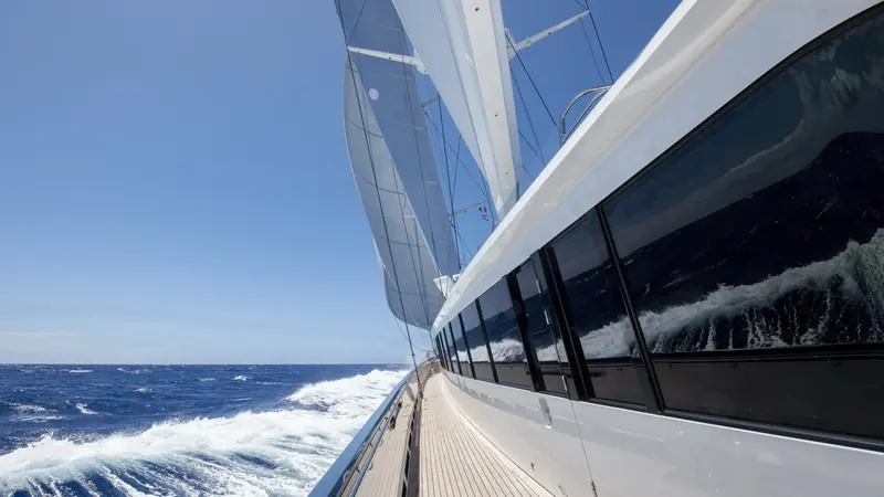 Bow wave curling away under a reefed headsail, the mainsail's carbon batten pockets visible against open sky.