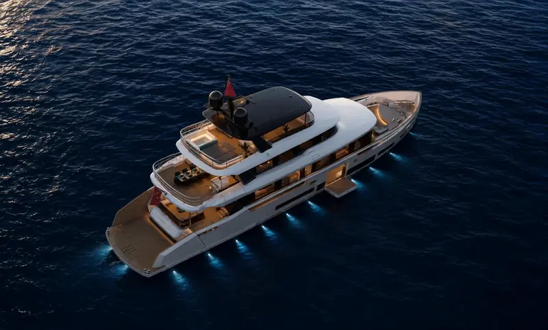 A blue-hour aerial shows the underwater lighting tracing the hull's full length, with the aft deck dining table and flybridge sunpad both lit for evening use.