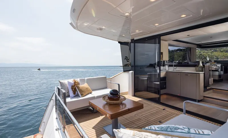 The main deck saloon opens on both sides through full-height sliding glass, so the galley and lounge share the same waterline view as the cockpit.