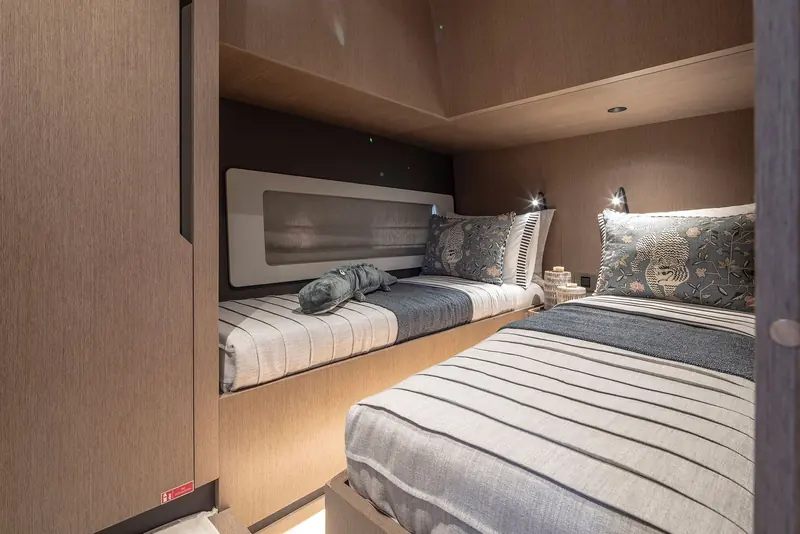 A guest cabin with an L-shaped berth rather than two singles, finished in the same pale oak as the saloon above it.