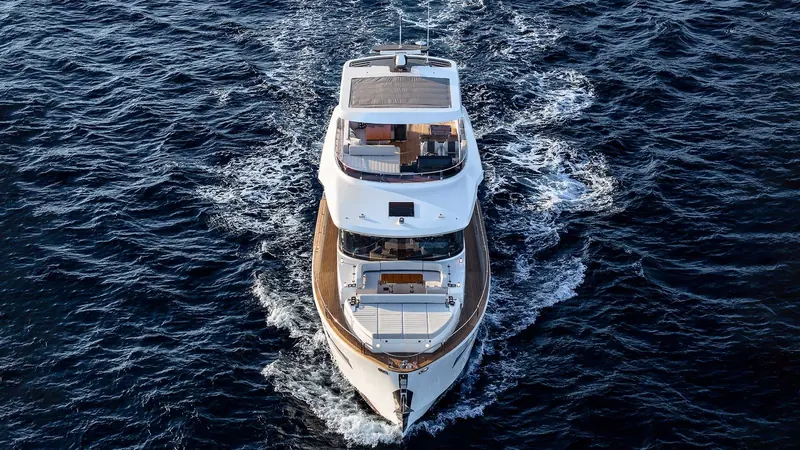 An aerial pass close to shore, the boat's wake curving as she turns rather than running in a straight test-track line.