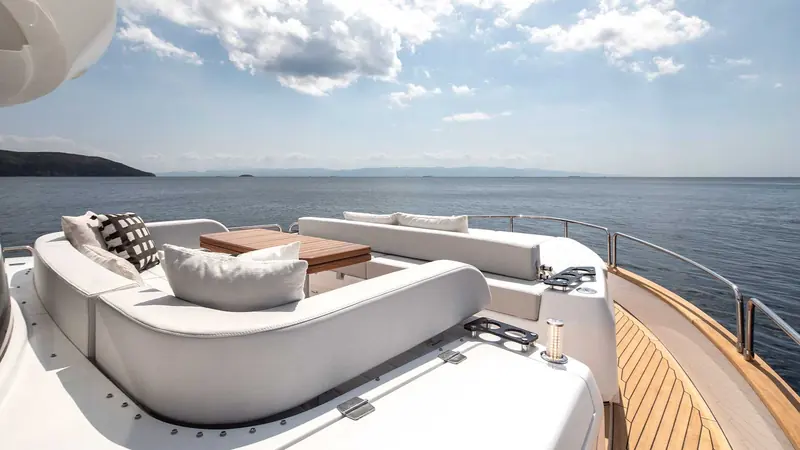 The flybridge aft lounge, cushions and a teak table set against open water with no chase boat or crew in frame.