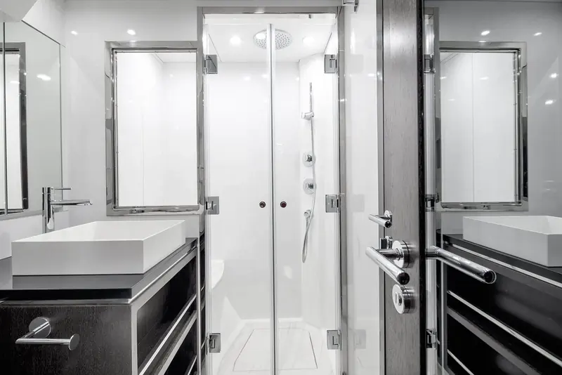 One of the ensuite bathrooms, a glass-walled shower and twin vanities finished in dark wood against white composite.
