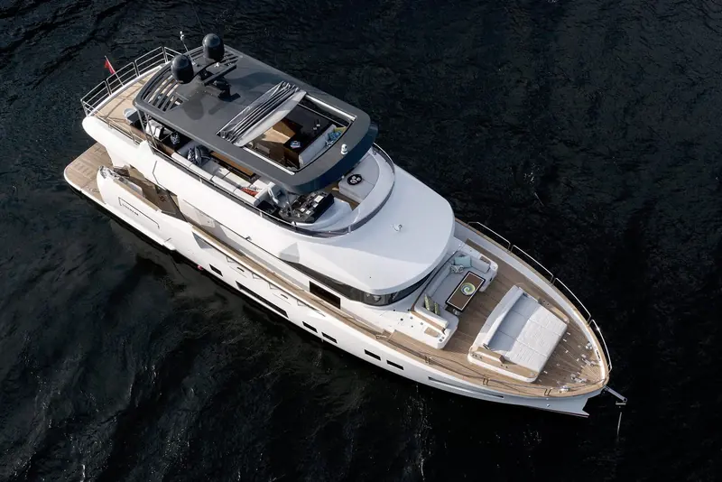 A three-quarter aerial at anchor showing the full flybridge layout, from the raised helm seats to the aft sunpad.