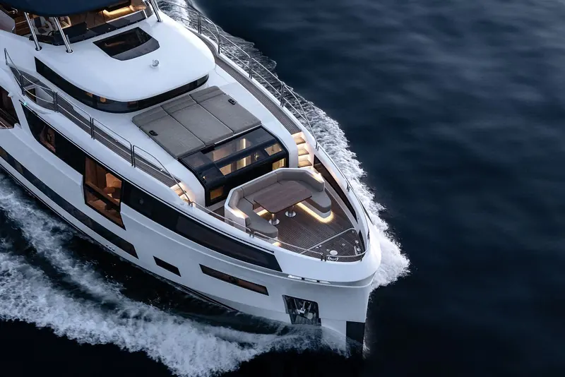 Underway at speed off a rocky Mediterranean coast, wake curling from the flat, low-freeboard hull that defines Sirena's line.