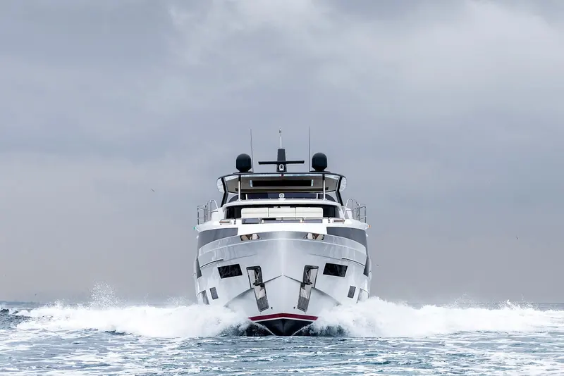Head-on into a beam sea under a heavy sky, the bow throwing solid spray clear over the anchor pockets - the boat's own sea trial, not a marketing calm.