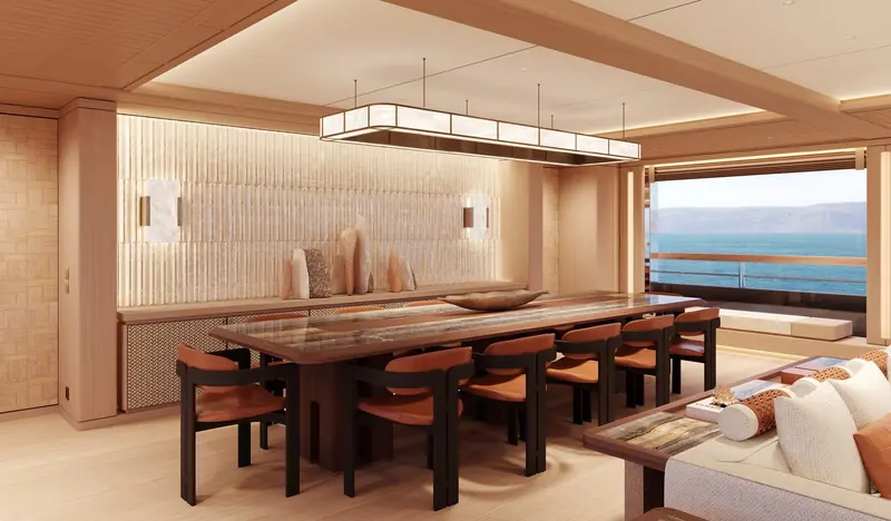 The formal dining table seats ten under a suspended onyx-panelled light fixture, with the aft deck and coastline visible through the open doors.