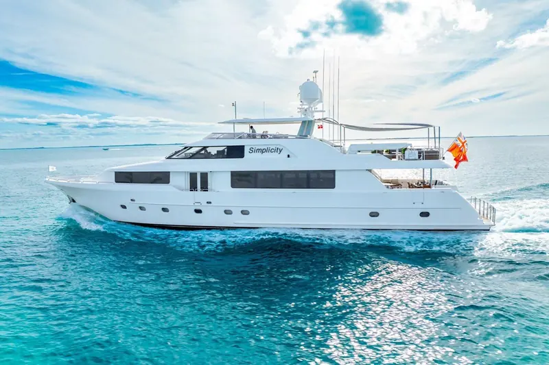 Simplicity, a 2012 Westport 112, underway with a clean bow wave breaking, her flag mast and open bridge deck visible aft.
