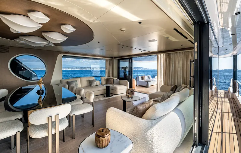 The main-deck saloon of an Arcadia A80, with dining table and lounge seating open to the water.