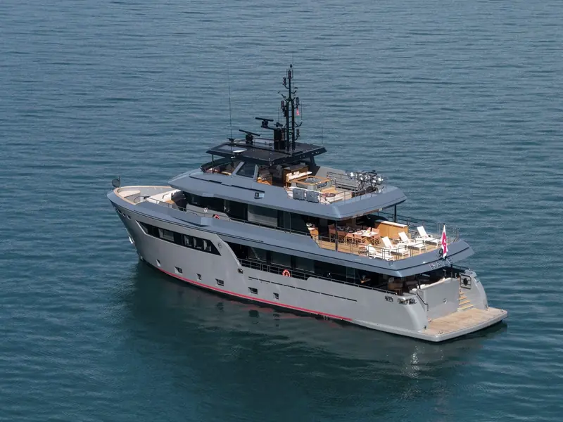 Underway in a sheltered bay, the red boot stripe and grey hull mark her out from the white-hulled convention most yards still default to.