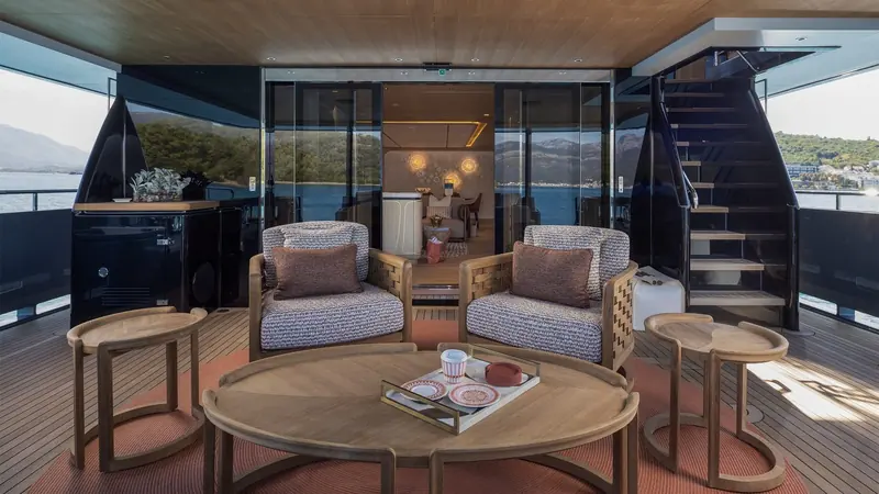 The aft deck lounge sits under cover between the cockpit and the saloon doors, furnished for the crew to serve breakfast without anyone leaving the shade.