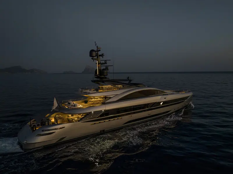 A Rossinavi hull built to Arrabito's naval architecture runs at dusk, her lit decks glowing against the darkening water.