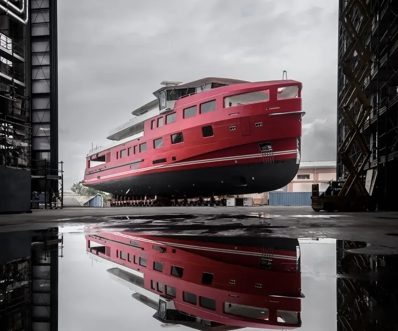 Akula's red hull is launched at Rossinavi's yard, reflected in the wet quayside below.
