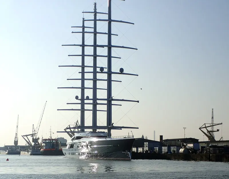 Black Pearl's masts catch the low sun at the Rotterdam yard, three free-standing carbon rigs whose loads had to be carried by a hull, not a styling brief.