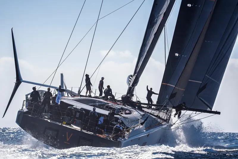Raven drives hard to windward, her dark sails loaded and spray breaking clean off the bow.