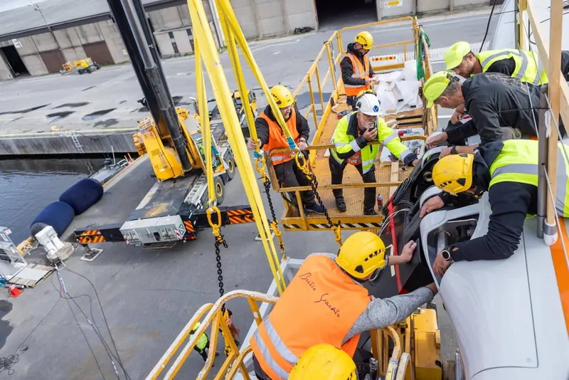 Yard workers secure lines during Raven's launch, the hull suspended over the harbour.