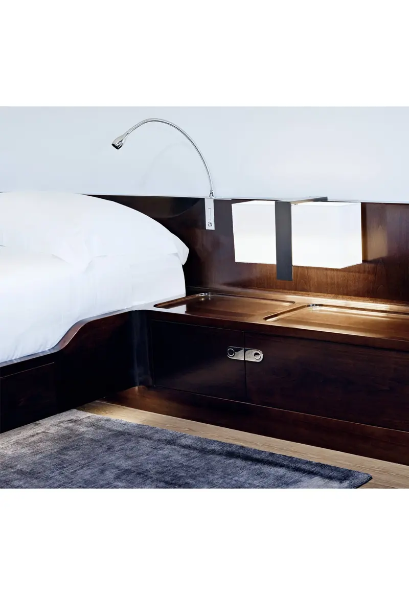 A bedside detail aboard Vertigo: a chrome flexible reading light and an inset walnut nightstand with catch-alls sunk directly into the wood.