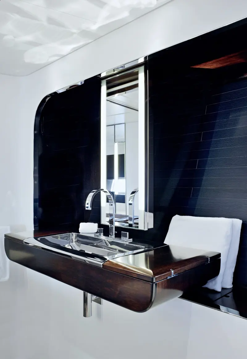 The ensuite vanity aboard Vertigo, its backlit mirror set into a curved dark-oak surround above a chromed sink for a spa-like, minimal wash area.