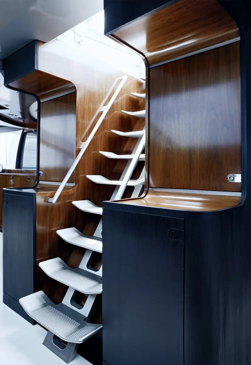 A companionway aboard Vertigo, its perforated aluminium treads folding down through a walnut-panelled stairwell in Liaigre's signature joinery.