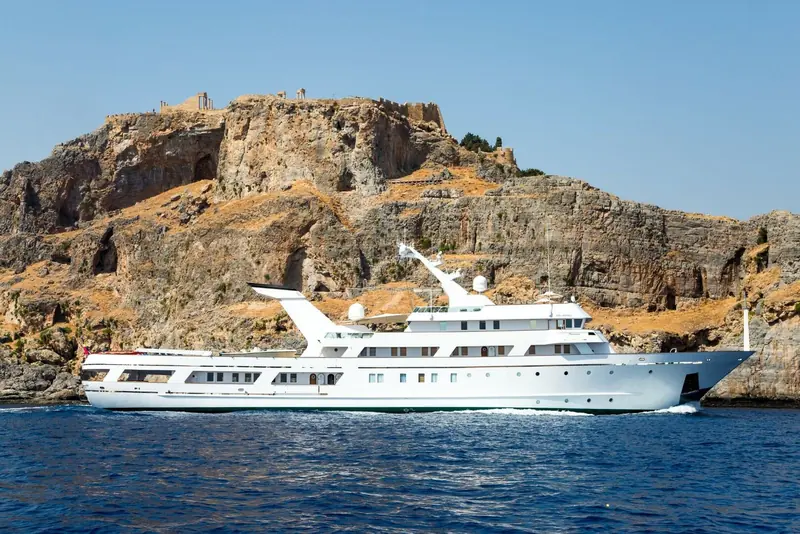 Esmeralda passes a rocky headland, her white hull and raked bow unmistakable from the 1981 delivery.