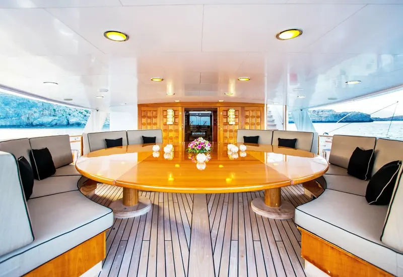 A shaded dining table is set on Esmeralda's deck, the coastline visible beyond the rail.