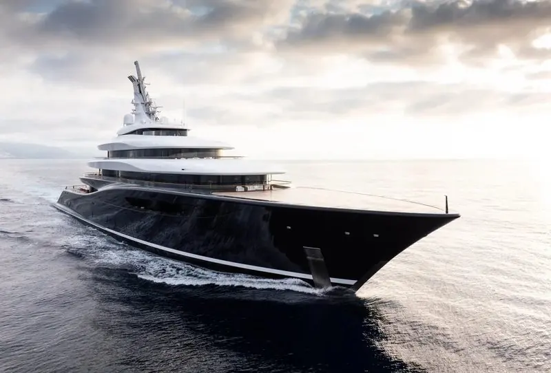 A dark hulled motor yacht runs through soft evening light with the coast low astern.