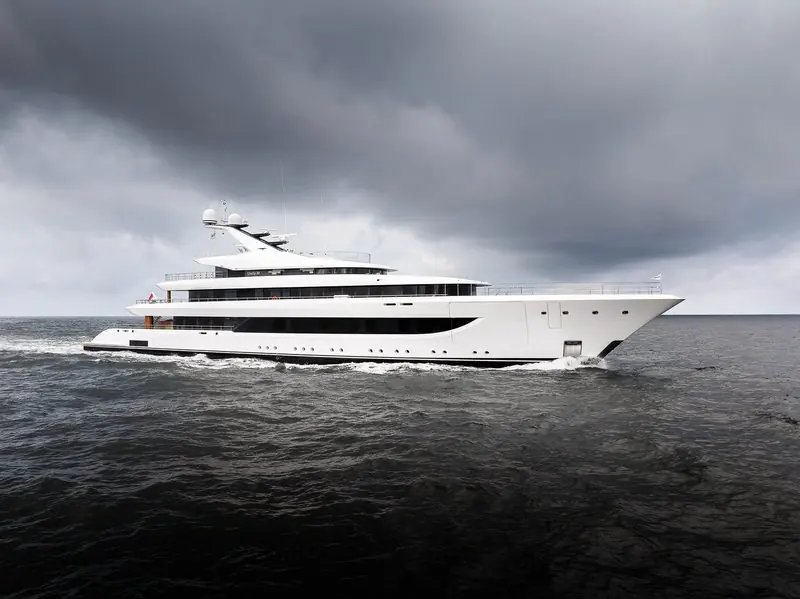 Storm cloud presses down as a white motor yacht pushes through a grey sea.