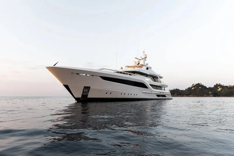 Mirror calm water holds the reflection of a white motor yacht off a wooded headland.