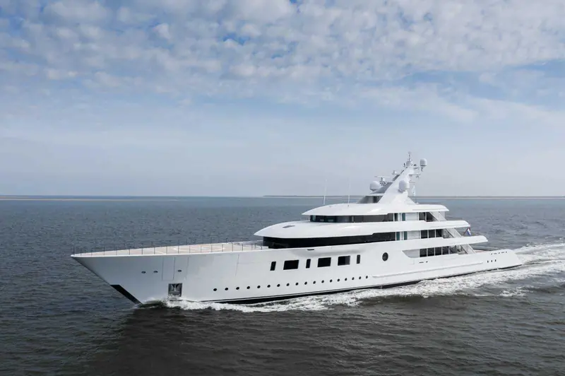 A De Voogt-drawn Feadship running fast off a low sandbar coast, helideck forward and full displacement hull leaving barely a wake at speed.